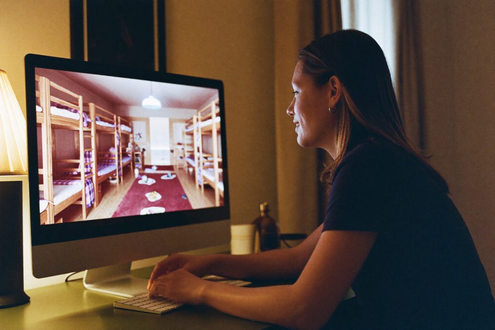 A student studies a virtual tour of a bunk-bed dorm room on a desktop monitor